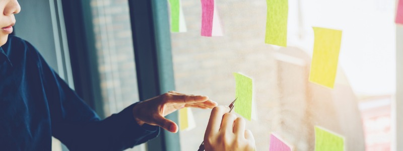 coworkers write on post-it notes that are posted on a window | building out your Accountability Chart